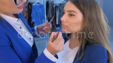 化妆师在美容院将唇彩用刷子涂在女模特的嘴唇上。